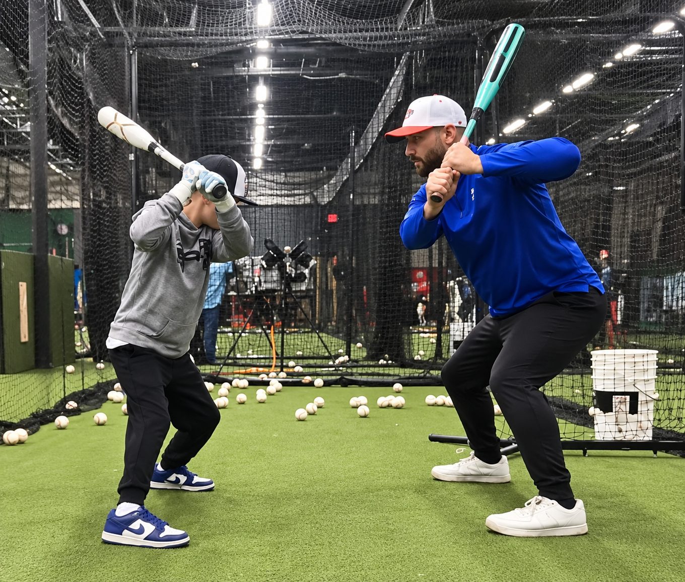 Coach Steve demonstrating a batting stance alongside Niall during a hitting lesson in an indoor batting cage. Niall and Coach Steve Training in Batting Cage