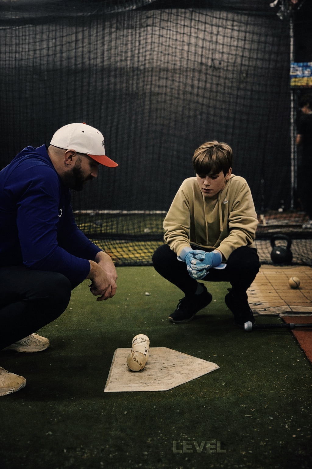 Coach Steve kneeling beside a hitter at home plate, working through the plan for the at-bat